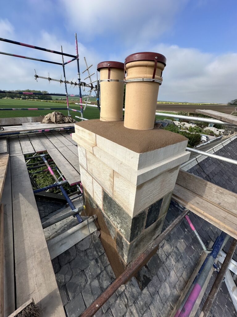 Rebuilt sandstone chimney stack with two chimney pots on the scaffold