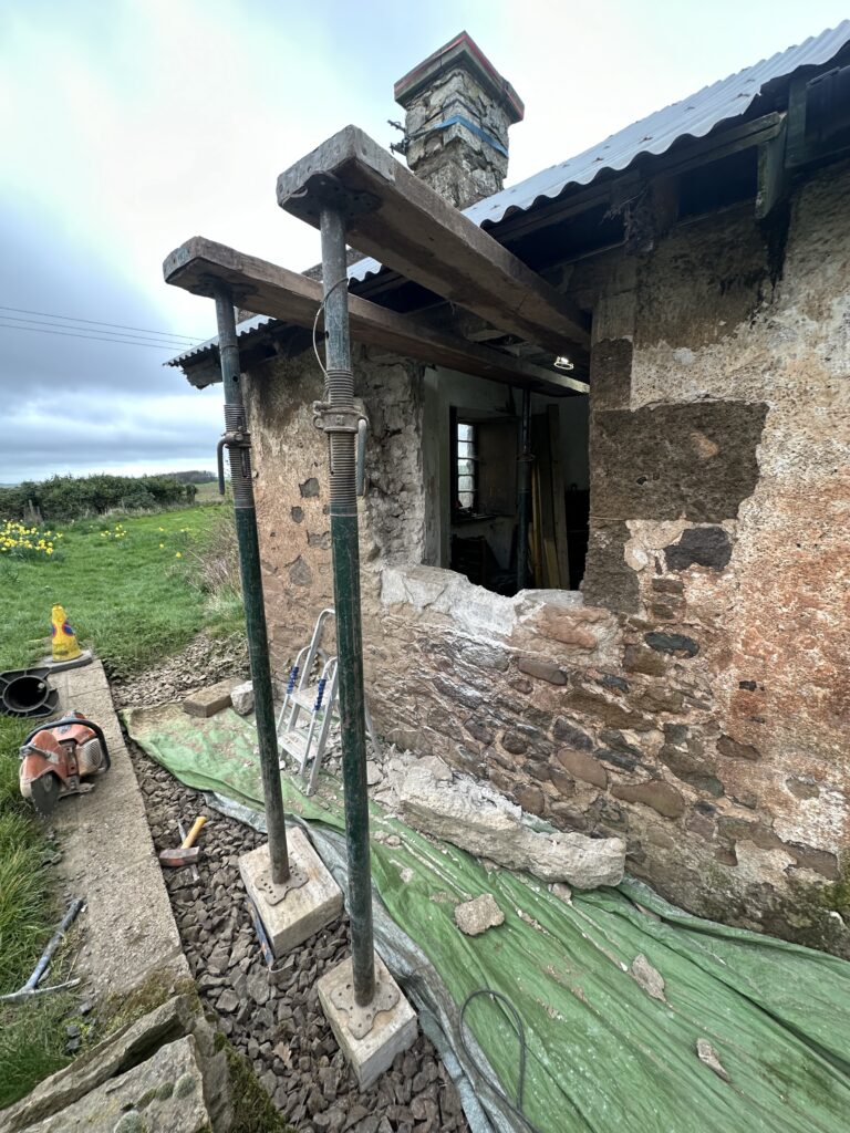 Collapsed stone outbuilding wall propped during restoration at West Lodge