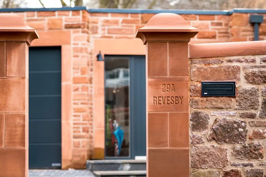 Red sandstone gate pillar carved with the house name beside a modern door